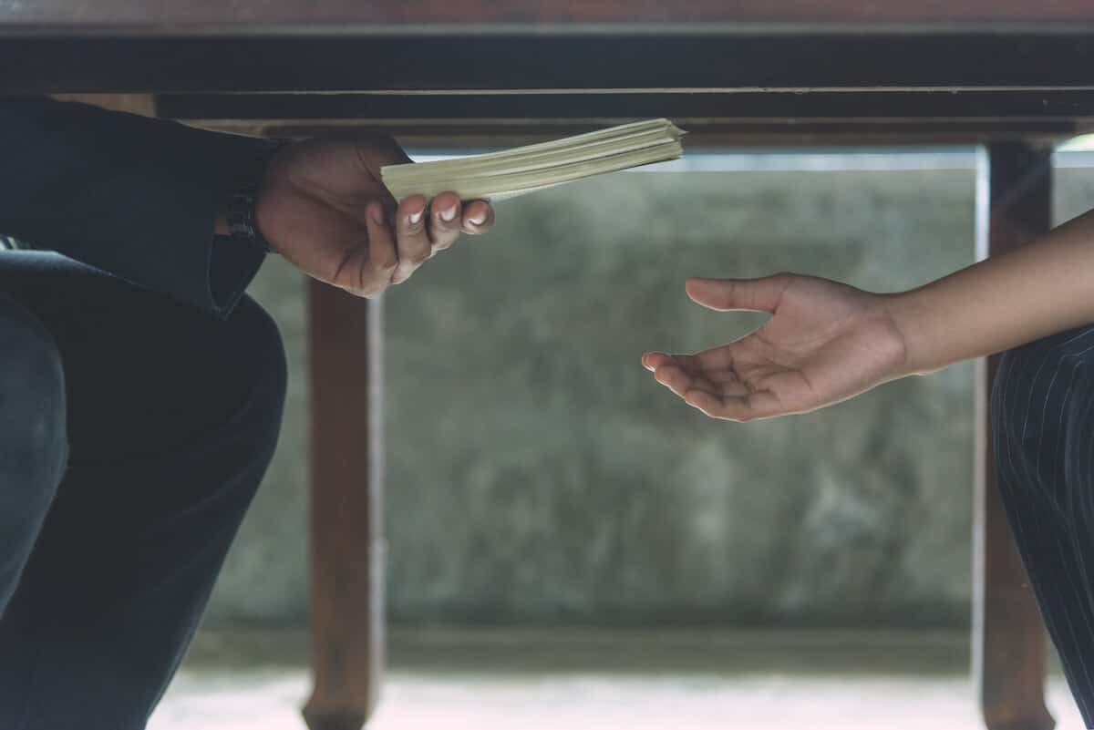 Person handing bribe money under a table