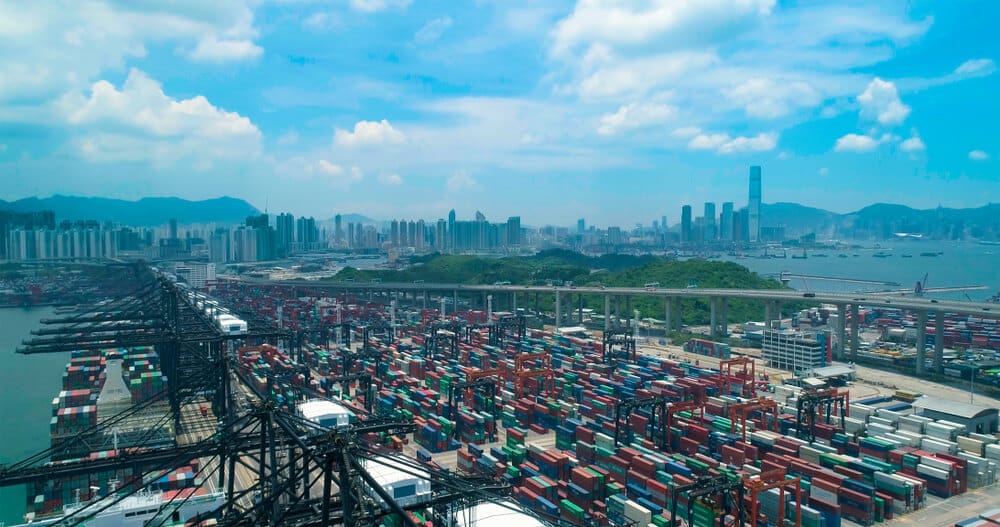 Port in Hong Kong with shipping containers and boats with a skyline of the city in the background.